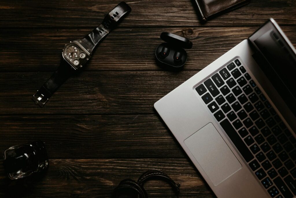 Top view of a sleek workspace featuring a laptop, watch, and earphones on a wooden table.