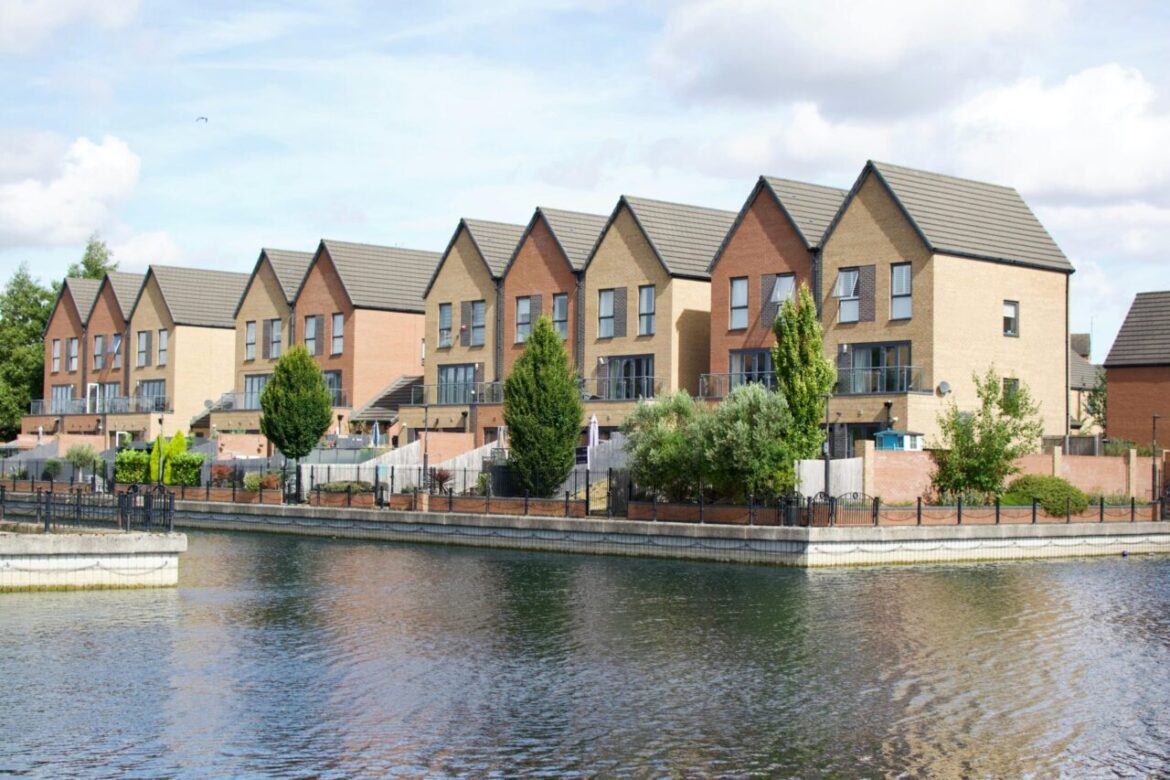 Row of modern townhouses by a waterfront under a bright sky, showcasing urban living.