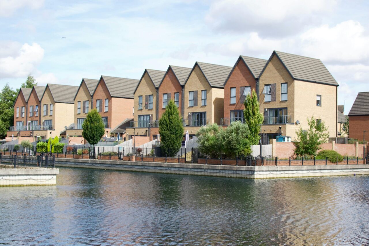 Row of modern townhouses by a waterfront under a bright sky, showcasing urban living.